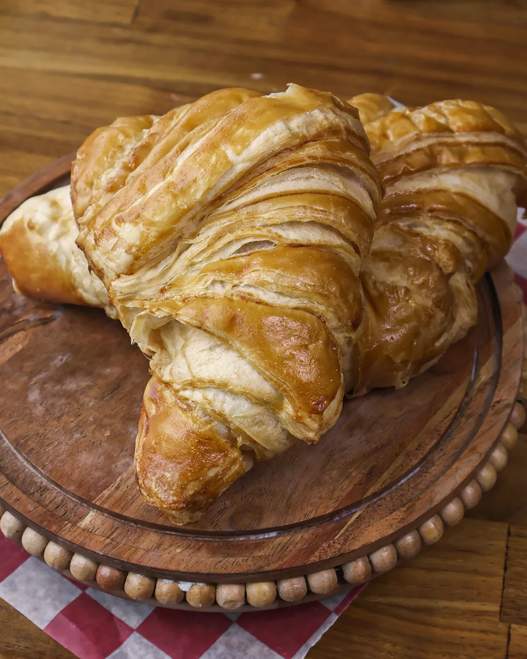 389424d5-3865-4f0e-9b8b-41b9f2dd1a5a.webp Golden-brown flaky pastries on a beaded wooden serving board with checkered paper